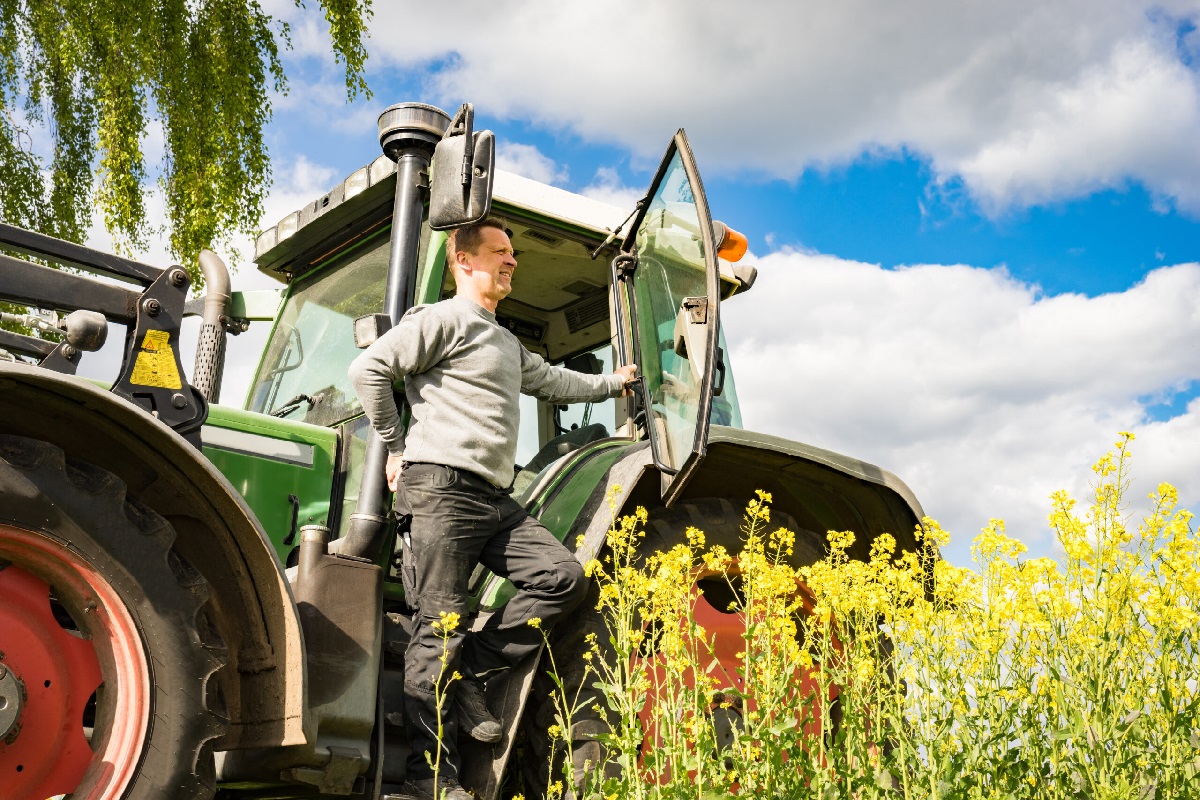 EU-kontroll på traktor. Traktor og fører i en gul eng med blå himmel, skyer og sollys